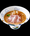 RAIJIN's Gyokai Tonkotsu Shoyu Frozen Ramen with pork slices in an ornate bowl on black background