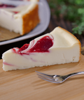 Slice of creamy strawberry swirl cheesecake on a wooden board with fork, featuring vibrant strawberry swirls and rich flavor.