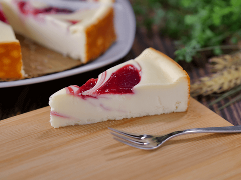 Slice of creamy strawberry swirl cheesecake on a wooden board with fork, featuring vibrant strawberry swirls and rich flavor.