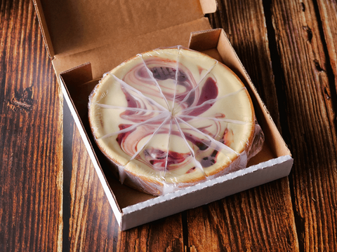 Strawberry Swirl Cheesecake in a box on wooden table, featuring vibrant strawberry swirls and creamy cheesecake.