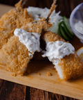 Breaded Aji Fry (Horse Mackerel) topped with sauce served on a wooden board with a lemon wedge and cucumber slices