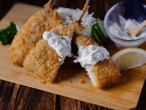 Breaded Aji Fry (Horse Mackerel) topped with sauce served on a wooden board with a lemon wedge and cucumber slices